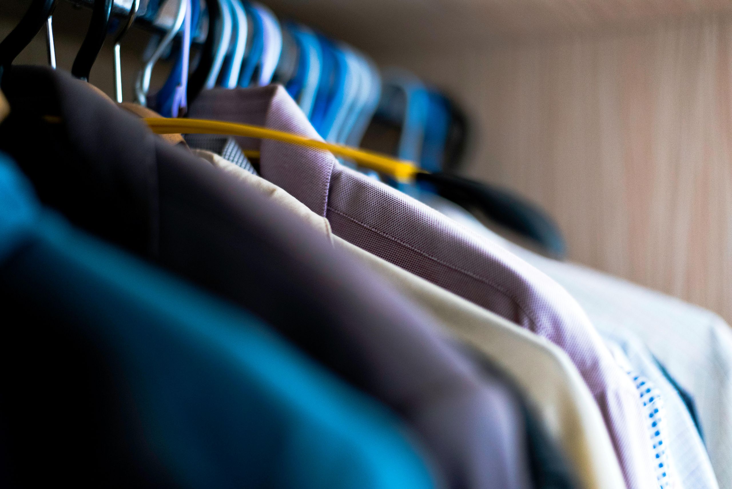 Close-up of several shirts hanging on plastic hangers in a closet, ideal for preparing your winter wardrobe—notice the crisp collars as you decide what to dry clean first. The shallow depth of field draws attention to the care behind clothing selection.