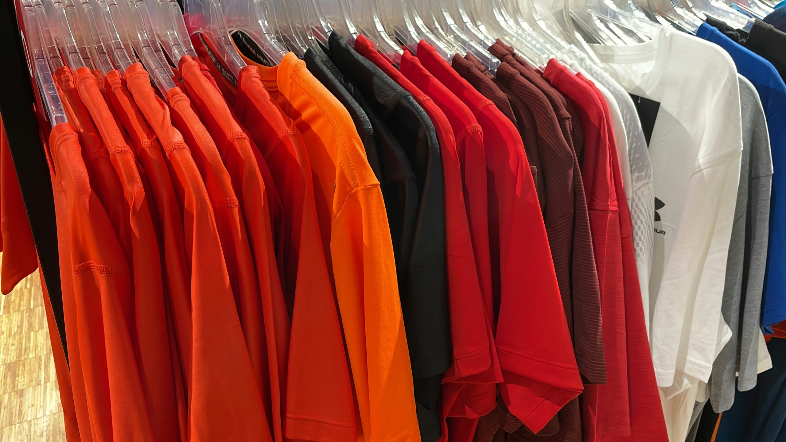 A row of short-sleeve t-shirts in various colors, freshly cared for with professional laundry cleaning, hang on clear plastic hangers on a clothing rack in a store.