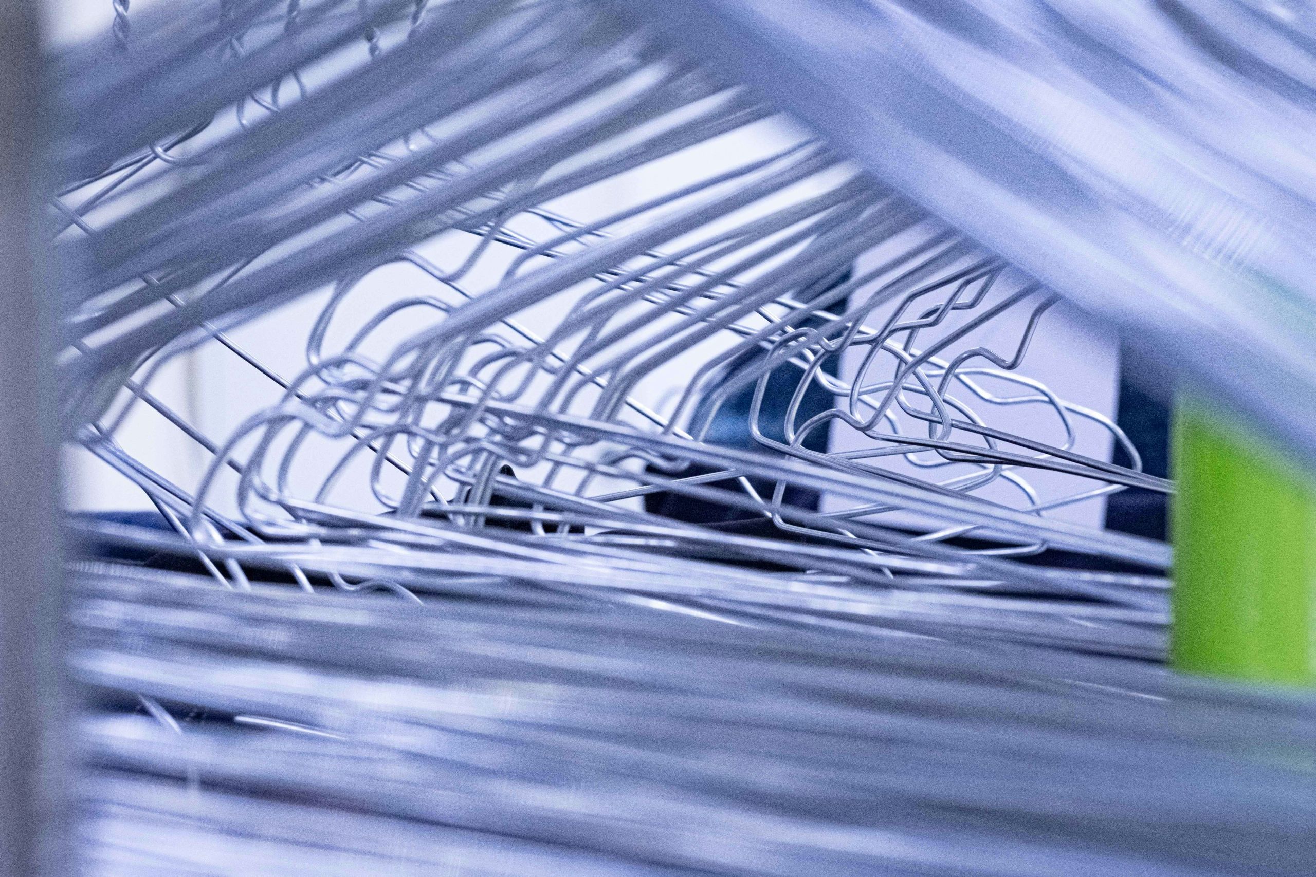 A close-up view of a chaotic stack of silver wire hangers, some twisted and overlapping, creates an abstract and tangled arrangement—evocative of the rush and bustle of same day dry cleaning.