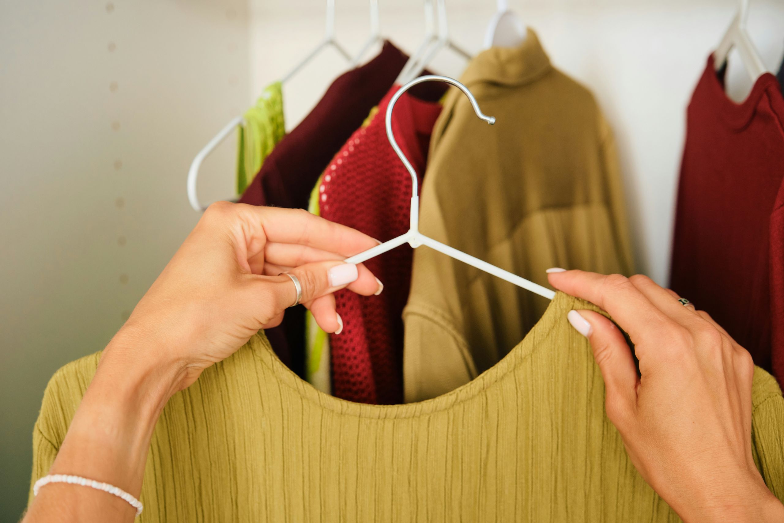 A person showing garment care, holds a green shirt on a white hanger in front of several colorful clothes hanging in a closet.